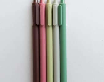 May include: Five pens in different colors: brown, pink, light green, gray, and green. The pens are all the same size and shape, and they are arranged in a row from left to right.