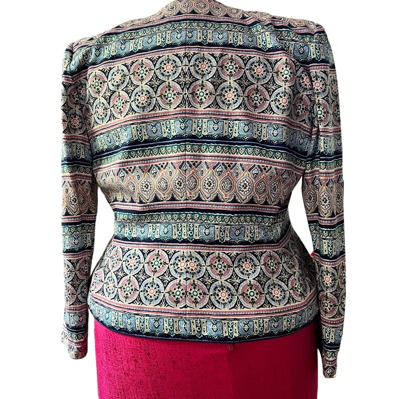 Peut inclure: Une veste &agrave; motifs au design vibrant. La veste pr&eacute;sente un m&eacute;lange de couleurs, dont le marine, le rose et le sarcelle, dispos&eacute;es en motifs circulaires et ray&eacute;s r&eacute;p&eacute;titifs. La veste a des manches longues et une coupe ajust&eacute;e, avec un bas rouge.