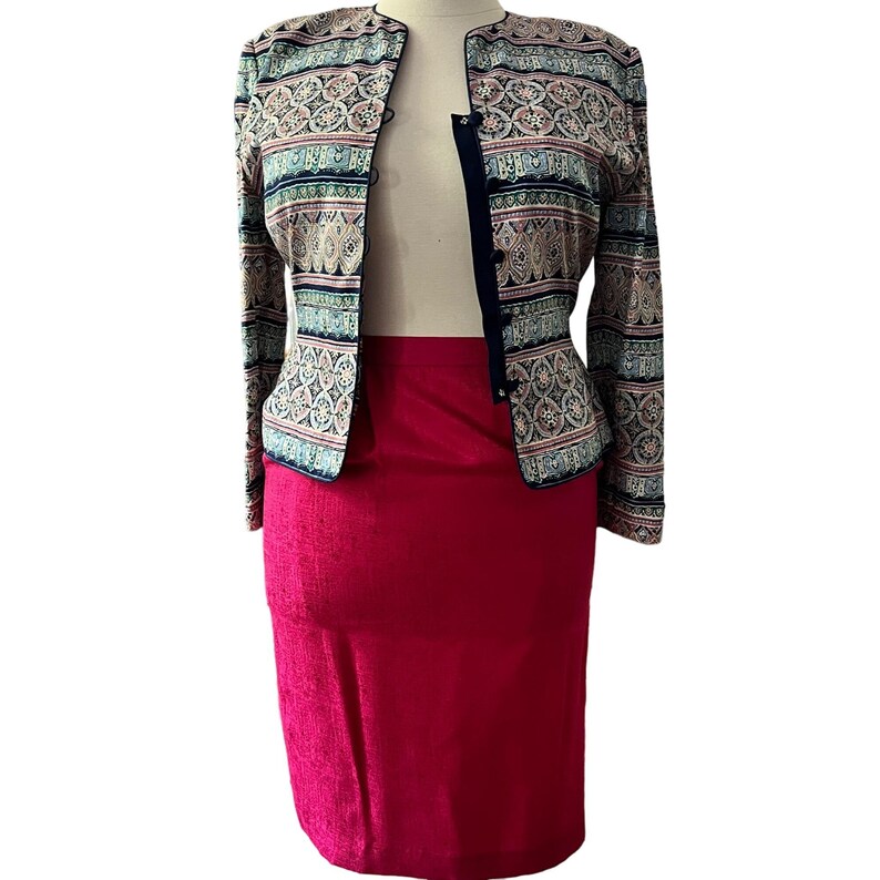 Peut inclure: Ensemble deux pi&egrave;ces compos&eacute; d'une veste &agrave; motifs et d'une jupe unie rouge vif. La veste pr&eacute;sente un motif d&eacute;taill&eacute; dans les tons de bleu, rose et beige. La veste est bord&eacute;e d'un liser&eacute; bleu marine.