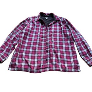 May include: A long-sleeve button-down shirt featuring a plaid pattern in shades of magenta, white, and dark gray. The garment includes a classic collar, a front button placket, and a dark gray interior lining visible at the neckline.