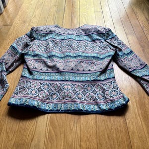 Peut inclure: Veste &agrave; manches longues orn&eacute;e d'un motif color&eacute; et complexe. La veste pr&eacute;sente des motifs g&eacute;om&eacute;triques bleus, roses et blancs. Le v&ecirc;tement a un col rond et est fait d'une mati&egrave;re douce.