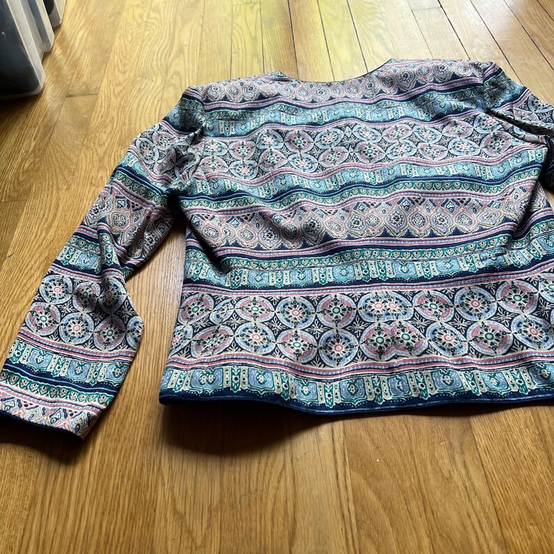 Peut inclure: Haut &agrave; manches longues avec un motif color&eacute; et complexe dans les tons de bleu, rose et vert. Le motif pr&eacute;sente des &eacute;l&eacute;ments g&eacute;om&eacute;triques et floraux. Le haut est en tissu doux et a une encolure ronde.