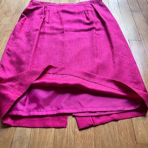 Peut inclure: Une jupe rose vif avec un tissu textur&eacute; et une fente &agrave; l'ourlet. La jupe a une taille ajust&eacute;e et un ourlet au genou. La doublure est rose fonc&eacute;. La jupe est faite d'un mat&eacute;riau brillant.
