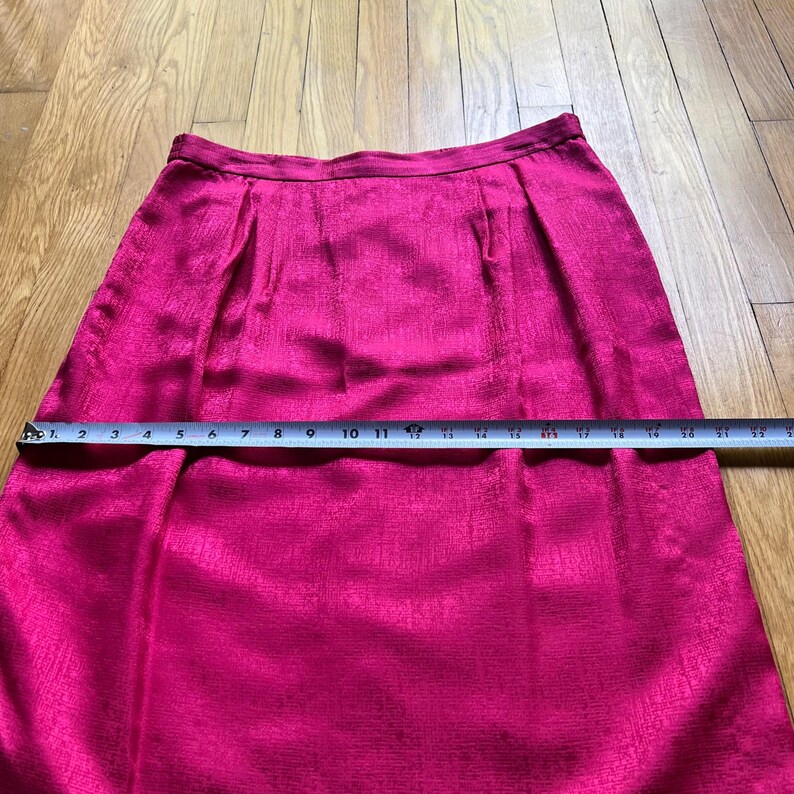 Peut inclure: Jupe rose vif avec une surface textur&eacute;e. La jupe est mesur&eacute;e avec une r&egrave;gle, indiquant une longueur d'environ 56 cm. Elle pr&eacute;sente des plis &agrave; la taille et une coupe l&eacute;g&egrave;rement &eacute;vas&eacute;e.