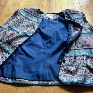 Peut inclure: Veste &agrave; motifs avec int&eacute;rieur bleu. La veste pr&eacute;sente un motif cachemire dans les tons de bleu, rose et vert. La veste a une encolure ronde et une fermeture &agrave; boutons. La doublure est de couleur bleu fonc&eacute; uni.