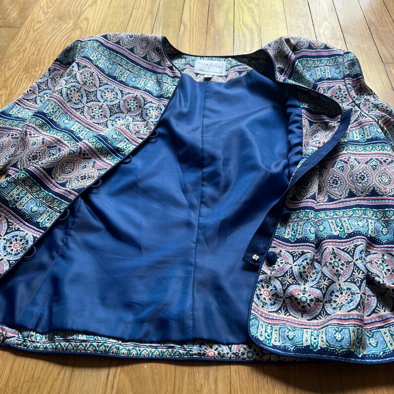 Peut inclure: Veste &agrave; motifs avec int&eacute;rieur bleu. La veste pr&eacute;sente un motif cachemire dans les tons de bleu, rose et vert. La veste a une encolure ronde et une fermeture &agrave; boutons. La doublure est de couleur bleu fonc&eacute; uni.