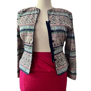 Peut inclure: Veste &agrave; motifs avec bordure et boutons bleu marine. La veste pr&eacute;sente un motif r&eacute;p&eacute;titif dans les tons rose, bleu et beige. Elle est associ&eacute;e &agrave; une jupe rouge vif. La veste est pr&eacute;sent&eacute;e sur un mannequin.
