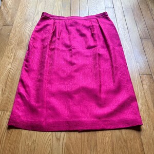 Peut inclure: Une jupe fuchsia vif avec un tissu textur&eacute;. La jupe a une silhouette trap&egrave;ze classique, avec des plis &agrave; la taille et un ourlet au genou. Le tissu brillant ajoute une touche d'&eacute;l&eacute;gance.
