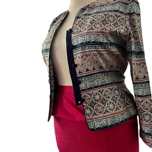 Peut inclure: Veste &agrave; motifs avec une jupe rouge. La veste pr&eacute;sente une bordure noire et une fermeture &agrave; boutons. Le motif comprend des nuances de bleu, de rose et de beige. La jupe est rouge vif uni.