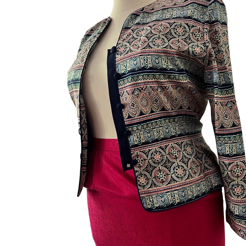 Peut inclure: Veste &agrave; motifs avec une jupe rouge. La veste pr&eacute;sente une bordure noire et une fermeture &agrave; boutons. Le motif comprend des nuances de bleu, de rose et de beige. La jupe est rouge vif uni.