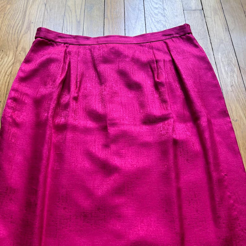 Peut inclure: Une jupe fuchsia vibrante avec un &eacute;clat subtil. La jupe pr&eacute;sente un devant pliss&eacute; et une ceinture ajust&eacute;e. Le tissu a un aspect textur&eacute;, ajoutant de la profondeur &agrave; la couleur unie. La jupe est de style genou.