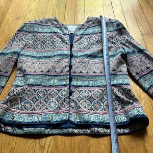 Peut inclure: Veste &agrave; motifs avec une bordure et des boutons bleu marine. La veste pr&eacute;sente un motif color&eacute; avec des formes g&eacute;om&eacute;triques roses, bleues et vertes. La veste mesure environ 63,5 cm de long.