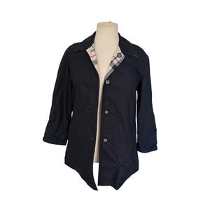 May include: A dark navy jacket with three-quarter length sleeves and a button-up front. The interior collar lining features a classic plaid pattern in red, white, and beige. The jacket is displayed on a mannequin.