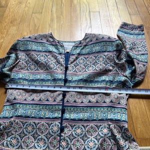 Peut inclure: Une chemise boutonn&eacute;e &agrave; motifs avec un col rond. La chemise pr&eacute;sente un motif r&eacute;p&eacute;titif de cercles et de formes g&eacute;om&eacute;triques dans des tons de bleu, de rose et de vert. La chemise mesure environ 58 cm de large.