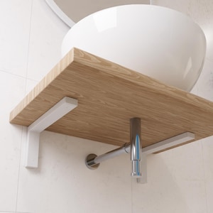 Könnte beinhalten: Ein weißes Keramikwaschbecken mit einem Holzregal und weißen Metallkonsolen. Das Waschbecken ist mit einem verchromten Rohr an der Wand befestigt.