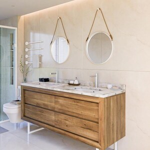 May include: A double vanity with a natural wood finish, four drawers, and a white marble countertop featuring two integrated sinks and silver faucets. Two round mirrors with white frames and brown leather hanging straps are mounted above the vanity.