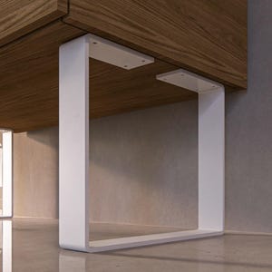 Può includere: Piedini da tavolo quadrati in metallo bianco con una piastra di montaggio rettangolare. I piedini sono fissati a una superficie in legno.