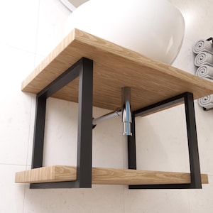 Peut inclure: Une vasque de salle de bain en bois avec un lavabo en céramique blanche et un cadre en métal noir. La vasque a une étagère inférieure pour le rangement.