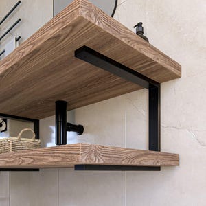 Peut inclure: Une étagère en bois avec des supports en métal noir. L'étagère est fixée au mur et a un dessus et un dessous en bois. Les supports sont en forme de L et ont une finition noire.