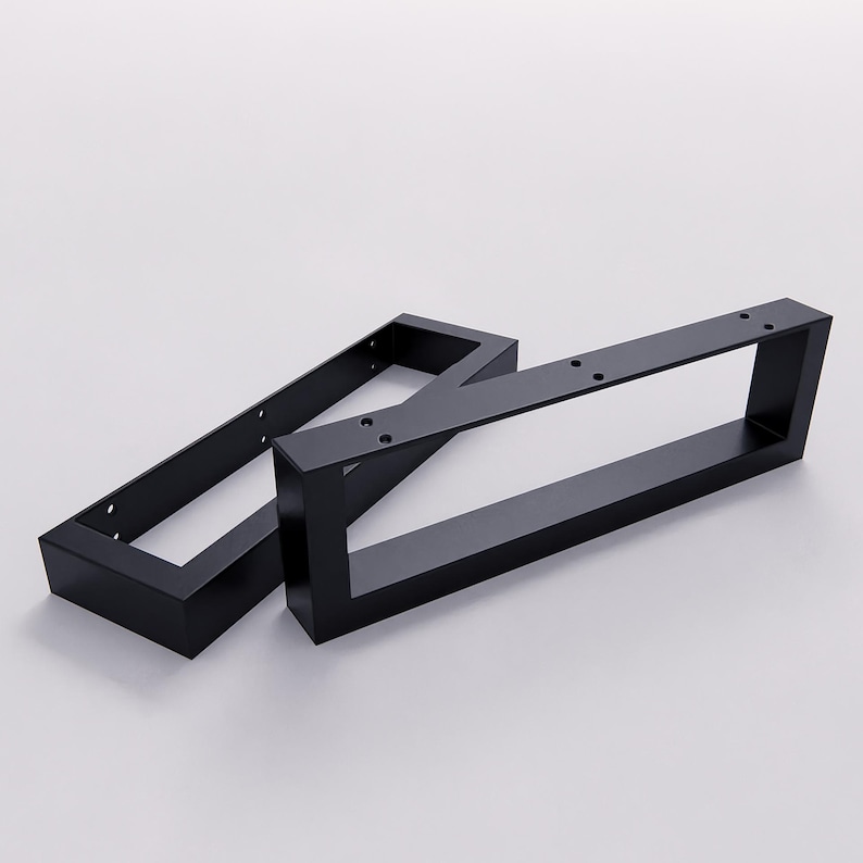 May include: Two rectangular black metal furniture legs featuring a hollow center design. Each leg has a flat top mounting plate with pre-drilled circular holes for attachment, constructed from solid matte black steel with clean, sharp edges.