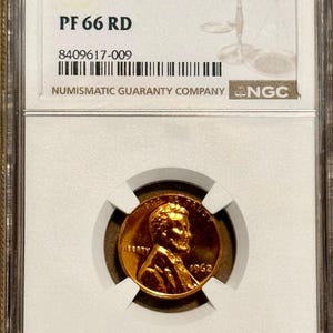 May include: A 1962 Doubled Die Obv 1C penny, graded PF 66 RD, encased in a Numismatic Guaranty Company holder. The coin features a portrait and the year 1962. The holder has a barcode and serial number.