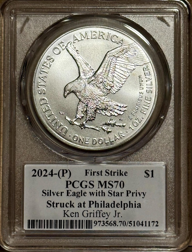 Peut inclure: Pi&egrave;ce d'argent am&eacute;ricaine de 2024, Silver Eagle, class&eacute;e PCGS MS70, avec un symbole d'&eacute;toile, dans un &eacute;tui de protection. La pi&egrave;ce repr&eacute;sente un aigle aux ailes d&eacute;ploy&eacute;es et le texte "UNITED STATES OF AMERICA". L'&eacute;tiquette indique "First Strike" et "1 oz. Fine Silver".