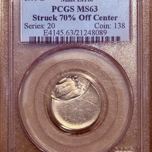 May include: A 1999-D 5C coin with a mint error, struck 70% off center, encased in a clear rectangular PCGS MS63 protective plastic slab. The label displays the text 1999-D, Mint Error, 5C, PCGS MS63, Struck 70% Off Center, Series: 20, Coin: 138, E4145.63/21248089.