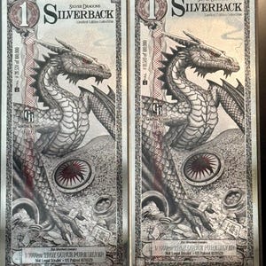 Könnte beinhalten: Zwei rechteckige Silverback-Sammlernoten in limitierter Auflage mit einer detaillierten Drachenillustration mit roten Augen. Die Noten zeigen den Text Silverback, 1/1000th troy ounce pure silver und Not Legal Tender sowie Seriennummern und das Jahr 2022.