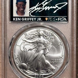 Peut inclure: Un objet de collection class&eacute; comprenant une carte de baseball de Ken Griffey Jr. et une pi&egrave;ce d'argent Walking Liberty de 2024. La carte est dans un bo&icirc;tier de protection avec le texte "LEGENDS OF LIFE" et une signature. La pi&egrave;ce repr&eacute;sente Lady Liberty.