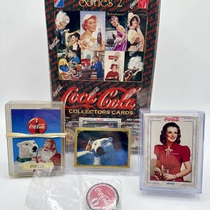 May include: A Coca-Cola Series 2 collectors card box featuring vintage advertisements, two plastic cases containing trading cards with polar bear and person illustrations, and a small round Coca-Cola metal tin in a clear plastic bag.