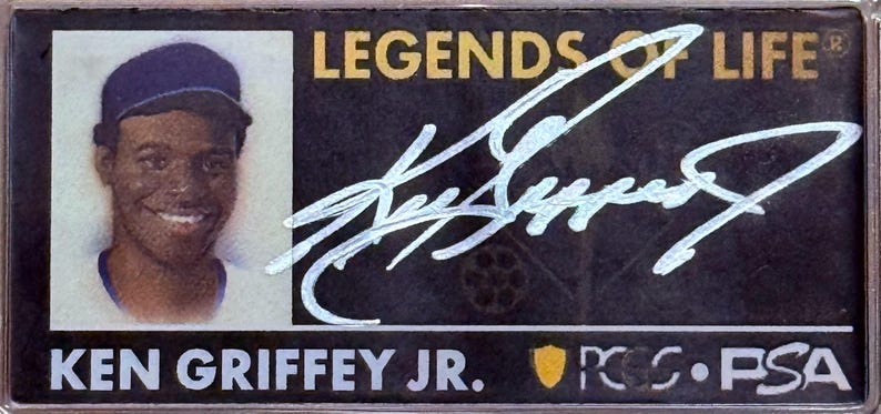 Peut inclure: Carte de collection de baseball avec Ken Griffey Jr. portant une casquette. La carte pr&eacute;sente un portrait de Griffey, une signature et le texte "LEGENDS OF LIFE" et "KEN GRIFFEY JR.". La carte est dans un &eacute;tui de protection.