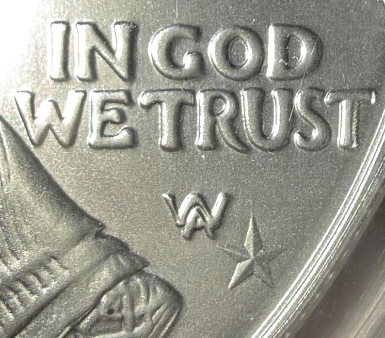 Peut inclure: Gros plan d'une pi&egrave;ce de monnaie argent&eacute;e avec les mots "IN GOD WE TRUST" en relief. La pi&egrave;ce pr&eacute;sente une marque d'atelier "W" et une &eacute;toile &agrave; cinq branches. Le bord de la pi&egrave;ce est visible.
