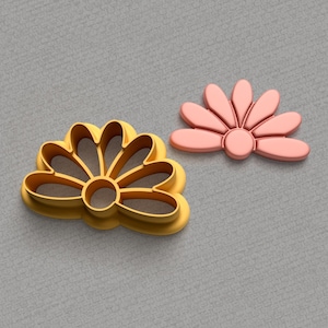 Puede incluir: Dos cortadores de galletas con forma de flor. El cortador de la izquierda es dorado y el de la derecha es rosa.