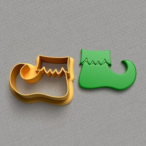 May include: Two elf shoe cookie cutters, one gold and one green. The gold cutter is open and the green cutter is closed.