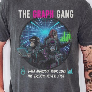 May include: Dark grey t-shirt featuring the text "THE GRAPH GANG" above a circular graphic of three cartoon apes. The graphic includes the text "DATA ANALYSIS TOUR 2023" and "THE TRENDS NEVER STOP".