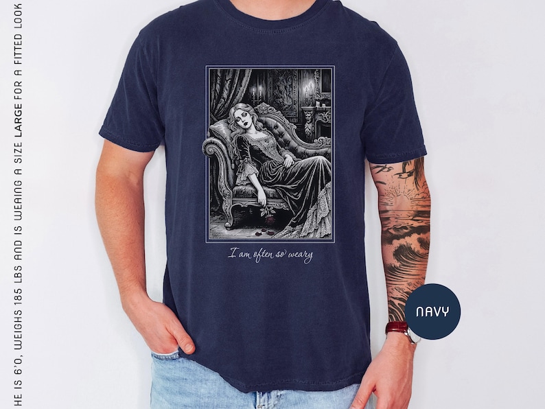 May include: Navy blue t-shirt featuring a black and white illustration of a woman reclining on a chaise lounge. The image includes the text "I am often so weary". The shirt is a size large.