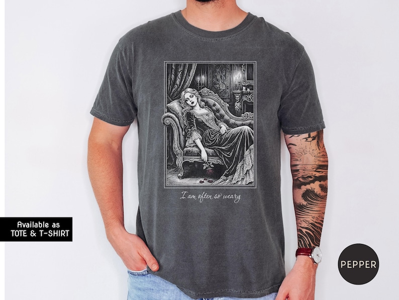 May include: Dark gray t-shirt featuring a black and white illustration of a woman reclining on a chaise lounge. The image includes the text "I am often so weary". Available as a tote and t-shirt.