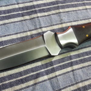 May include: A silver and brown double-edged dagger with a wooden handle. The dagger has a sharp point and a straight edge.