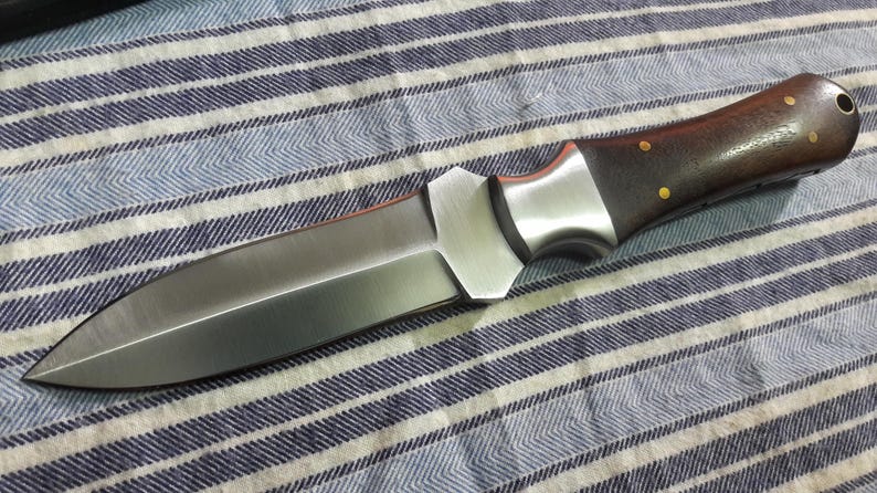 May include: A silver and brown double-edged dagger with a wooden handle. The dagger has a sharp point and a straight edge.