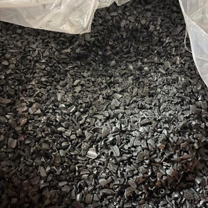May include: A close-up view of a large quantity of black plastic granules. The granules are irregularly shaped and appear to be recycled plastic.