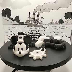 May include: A black and white 3D-printed Mickey Mouse head with a chef's hat, surrounded by other nautical-themed elements. The scene is set against a black and white backdrop of a steamboat on water, evoking a vintage cartoon aesthetic.