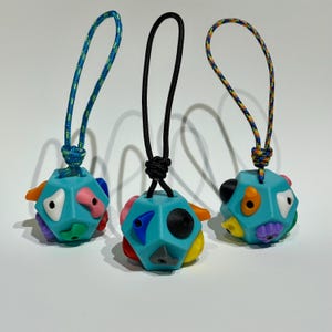 May include: Three colorful, multi-sided, blue, rubber toys with different colored shapes on each side. Each toy has a string loop attached to the top.