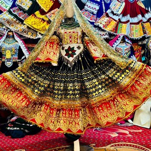 May include: A traditional black dress with gold and red embroidery. The dress features a detailed bodice, long sleeves, and a full skirt. A matching head covering and decorative belt complete the ensemble. The dress is displayed on a mannequin.