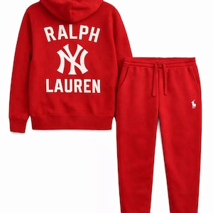 Puede incluir: Un conjunto rojo de sudadera con capucha y pantalón de chándal a juego. La sudadera con capucha presenta el texto "RALPH LAUREN" con un logotipo estilizado en la espalda. El pantalón de chándal tiene cintura con cordón y un pequeño logotipo en la pernera.