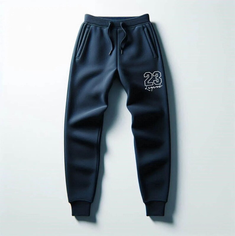 May include: Navy blue sweatpants with a drawstring waist and side pockets. The pants feature the number "23" and the word "Legend" in white lettering on the left leg. The pants are made of a soft material.