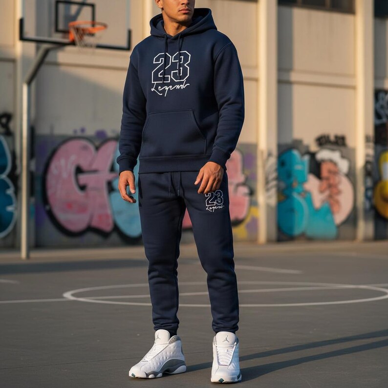 May include: Navy blue hoodie and sweatpants set with white "23 Legend" text. The hoodie has a front pocket and drawstring hood. The sweatpants have a matching logo on the left leg. The person is wearing white and gray sneakers.