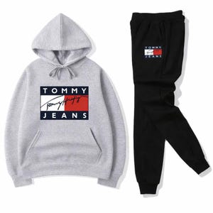 Puede incluir: Un conjunto de sudadera con capucha gris y pantalón de chándal negro. La sudadera con capucha presenta una capucha con cordón, un bolsillo delantero y el logotipo "TOMMY JEANS" en un diseño rectangular. El pantalón de chándal también tiene el logotipo "TOMMY JEANS".