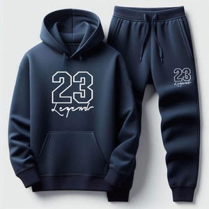 May include: Navy blue hoodie and sweatpants set. The hoodie features a front pocket and a hood. The number "23" and the word "Legend" are printed in white on both the hoodie and the sweatpants. The sweatpants have a drawstring waist.