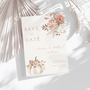 May include: A cream-colored wedding invitation with the text "SAVE the DATE" in gold. The invitation features floral and pumpkin illustrations in muted tones. The date "26.08.23" is displayed, along with the names "Lauren & Michael" and address details.