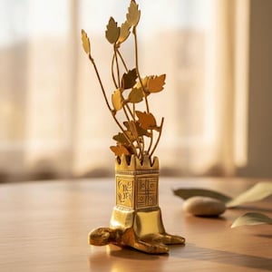 May include: A gold-colored metal turtle figurine featuring a square base with engraved symbols, including an Om and a swastika. The turtle supports a vertical arrangement of thin metal stems topped with flat, leaf-shaped cutouts.